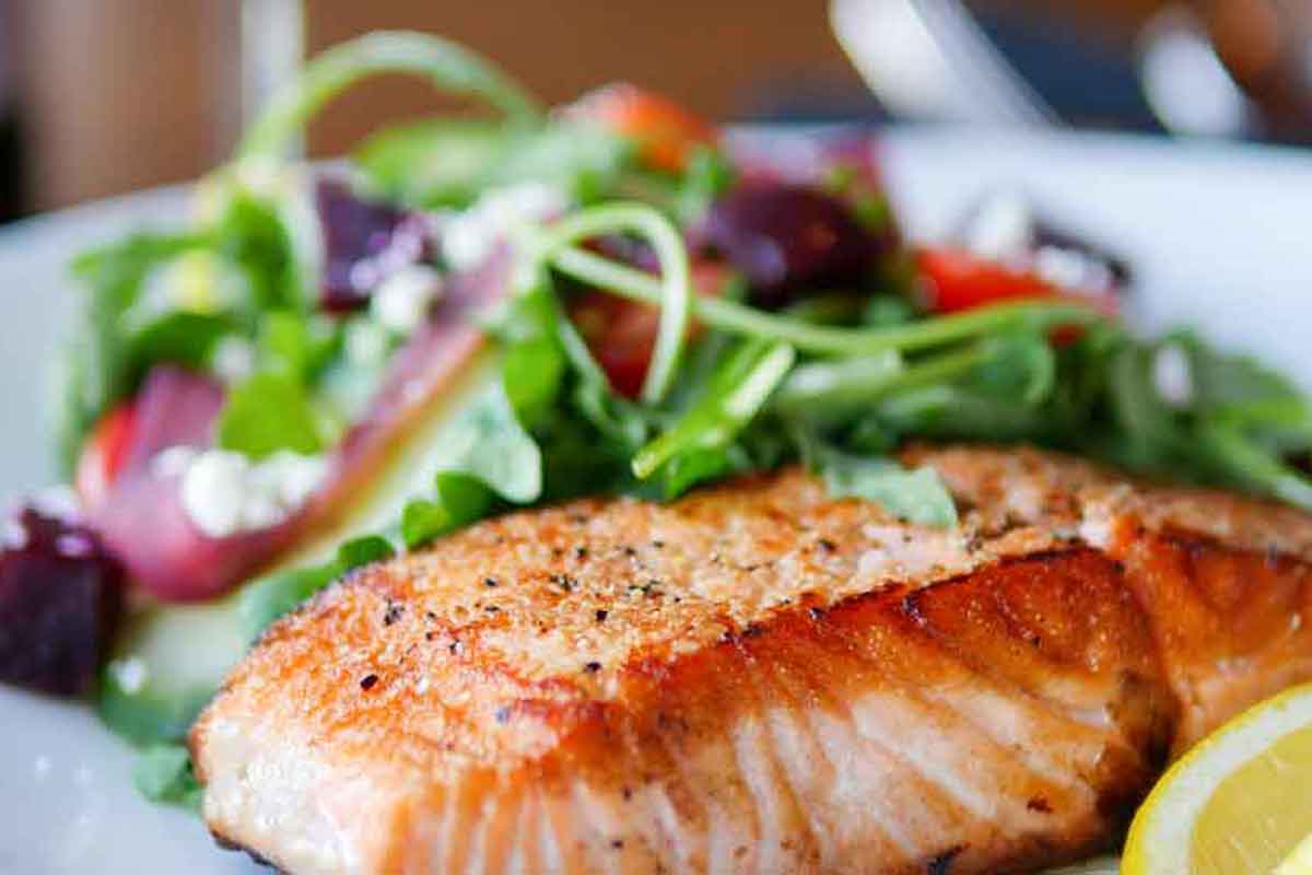 A piece of seasoned salmon cooked perfectly with a delicious fresh salad and a slice of lemon