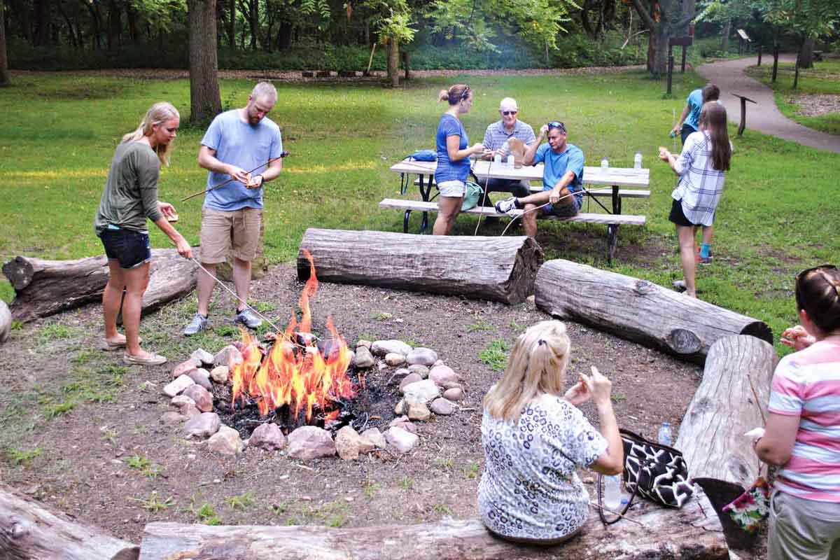 people roasting s'more during the daytime around a campfire with wooden log benches