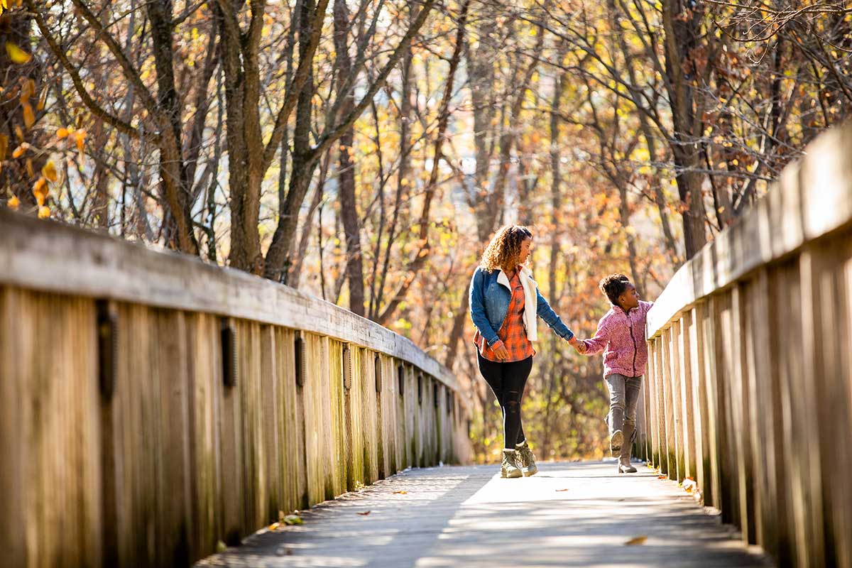 Mom and daughter walking on trail bridge in autumn