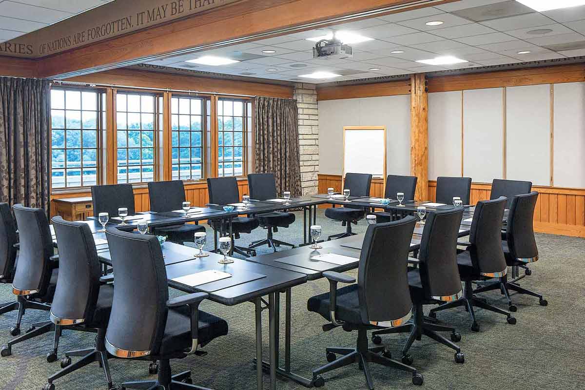 An executive meeting room with full-sized chairs, black table and water with window views