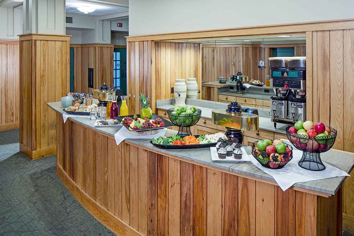 A picture of a fruit buffet with apples, cupcakes, coffee maker, juices, and assorted pastries