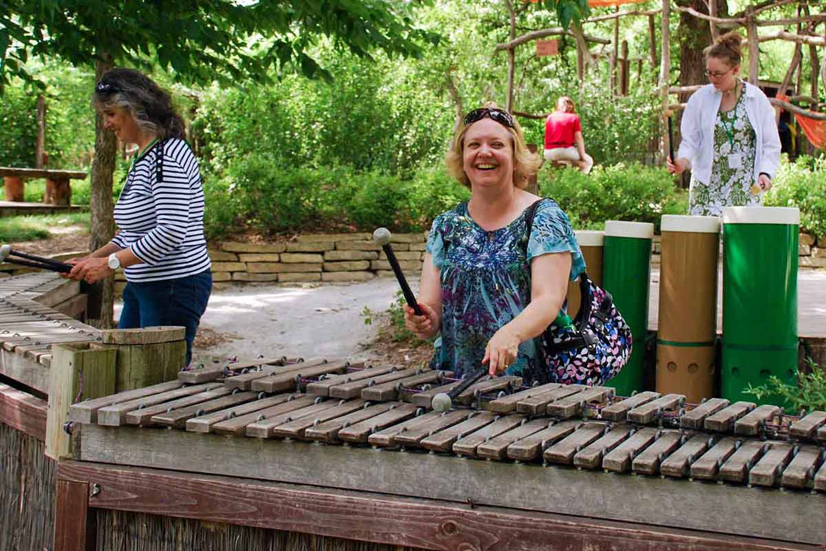People playing on three large outdoor xylophones